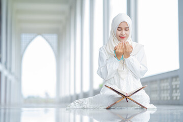 The image of an Asian Muslim woman in the Islamic religion in hijab in white color. reading the...