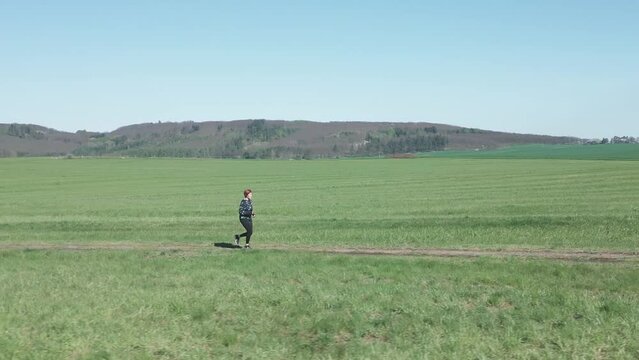 Wide, dynamic shot of a woman jogging along a dirt road in a vast landscape.