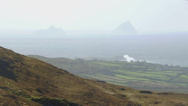 Skellig Michael in distance as waves crash on shore near houses