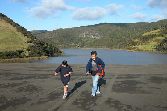 Father and teenage boy walking on Lake Wainamu sand dunes at Bethells beach. Auckland.