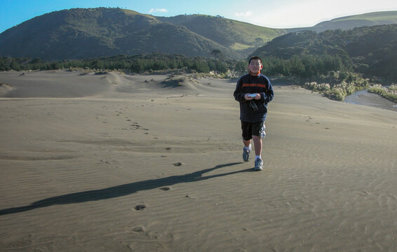 Teenage boy running on Lake Wainamu sand dunes at Bethells beach. Auckland.