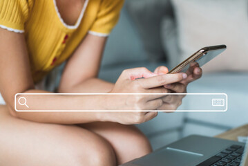 Fototapeta premium Young woman wearing yellow t-shirt sitting on sofa at living room use their smartphones to find out what interests them, to find ideas about networking and online learning with search bar icon.
