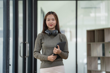 Smiling young Asian businesswoman holding a digital tablet standing in an office.