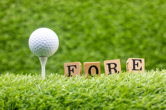 A golf ball with the word "FORE" writen on it is sitting on green grass. This is usually done to warn other golfers that somebody is about to hit the ball.