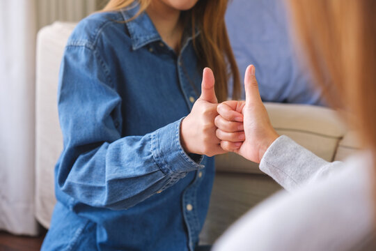 Closeup of a couple women making and showing thumbs up hand sign - Powered by Adobe