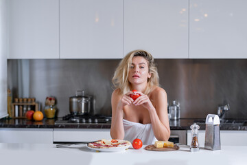 Woman with ingredients for pizza, cheese, sausage and tomato. Woman eating breakfast in a kitchen. Sexy housewife on morning. Housework.