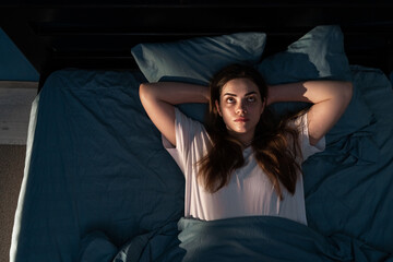 Stressed young woman on bed at night suffering from insomnia, top view. Depressed awake girl lying...