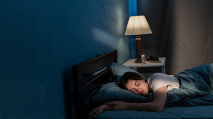 Young woman sleeping in soft bed in late at night. Lying cozily in bed, hugging a pillow. Girl...