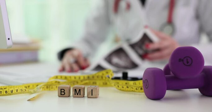 Dumbbell measuring tape and word BMI in wooden block and doctor. Healthy nutrition sport and human health