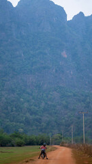 Guy riding his motorbike on a dirt path with luxurious mountain in background, Thakhek loop, Laos