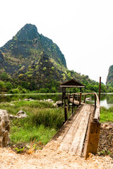 Luxurious mountain with vegetation next to a lake, with a little wooden hut and a bridge, Thakhek loop, Laos