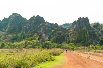 Dirt path with green fields and luxurious mountain in the background, Thakhek loop, Laos