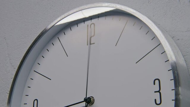 Static shot of white watch with metal frame hanging on the wall and showing time. Walking wall clock in office with modern design. Strict clock with fast running time pointer. Timelapse. Close up.