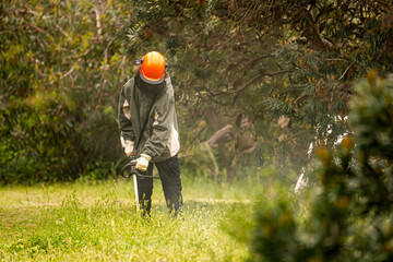 A worker in a protective suit mows the grass in the garden.