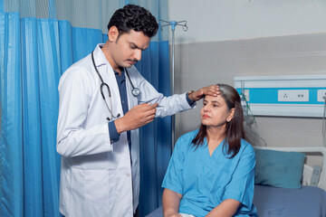 Indian doctor using thermometer while check up to patient at hospital.