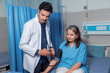 Indian doctor checking blood pressure of senior patients at hospital.