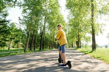 millennial guy on e-scooter outdoors, teenage boy standing on park on warm sunny day. Green transportation and urban lifestyle