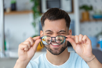 Young man holds glasses with diopter lenses and looks through them, the problem of myopia, vision...