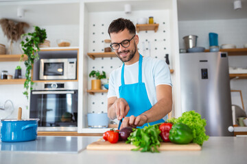 Handsome young man man stand at modern kitchen chop vegetables prepare fresh vegetable salad for dinner or lunch, young male cooking at home make breakfast follow healthy diet, vegetarian concept