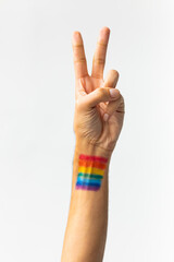 Close up of hand of biracial man showing peace sign with rainbow flag on white background