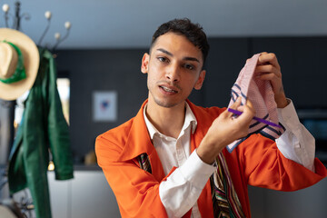 Happy biracial transgender fashion designer sitting at desk, holding fabric and having video call