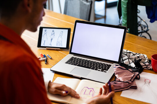 Close up of biracial transgender fashion designer using tablet and laptop with copy space on screen