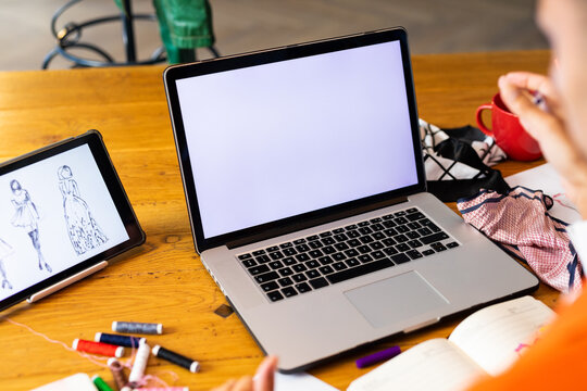 Close up of biracial transgender fashion designer using tablet and laptop with copy space on screen