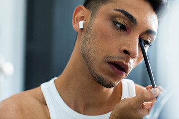 Biracial transgender man looking in mirror and putting on make-up, applying eyeshadow