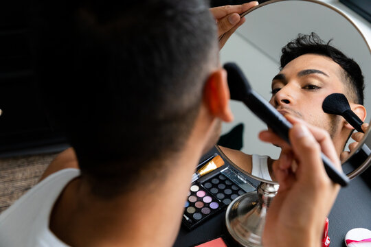 Biracial transgender man looking in mirror and putting on make-up, applying blush