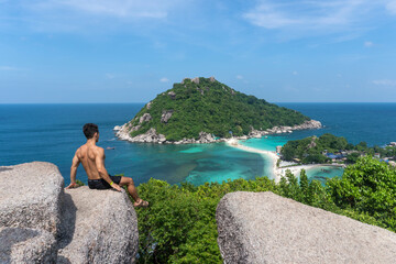 Guy with a swimshirt looking at an island from Koh Nang Yuan view point in Koh Tao island, Thailand.