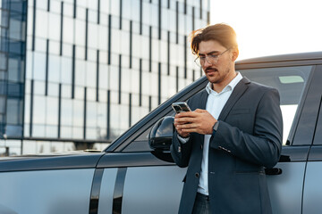 Young businessman standing near luxury car and using smartphone