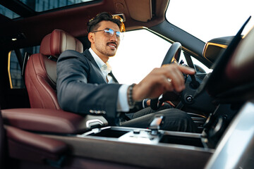 Young businessman in elegant suit driving luxury car