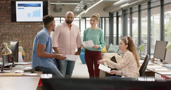 Diverse creative business colleagues with documents in discussion at casual office, in slow motion
