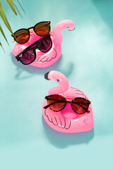 Trendy sunglasses of different design on inflatable flamingo on blue background with palm leaf....