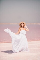 Fototapeta na wymiar Woman in pink salt lake. She in a white dress and hat enjoys the scenic view of a pink salt lake as she walks along the white, salty shore, creating a lasting memory.