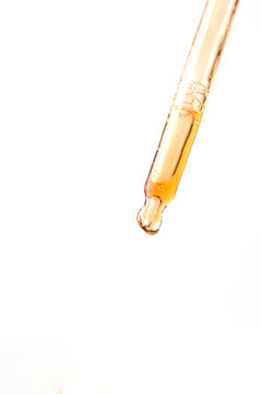 Cosmetic pipette with yellow liquid drop at isolated white background
