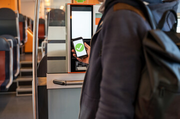 Person buying train ticket with smartphone from ticket machine. Holding phone with green check mark