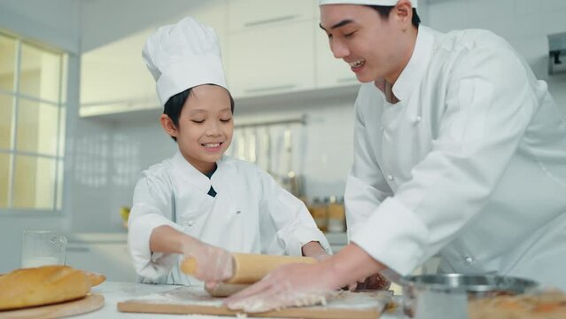 Asian chef man and boy in chef uniform cooking or baking together in kitchen room. Chef teaching little boy cooking or baking at freetime or holiday