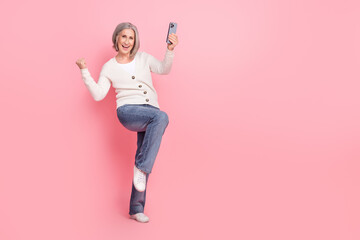 Full length photo of lovely retired lady raise fists celebrate success gadget wear trendy white garment isolated on pink color background