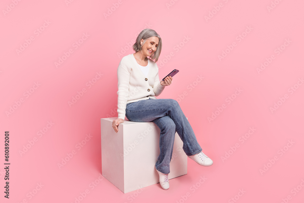 Poster Full size photo of attractive senior woman sitting cube hold device read news wear trendy white clothes isolated on pink color background