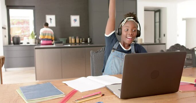 Happy african american girl using headphones and laptop rasing hand in online lesson, slow montion