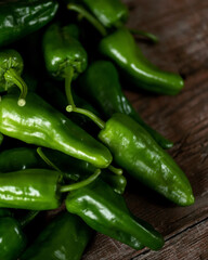 Green hot Padron pepper. Lot of ripe peppers on wooden surface. Pepper harvest. Pepper cultivation. Bright spices. Spicy food. Spanish pepper. Wooden background. Close-up. Soft focus. Top view. 