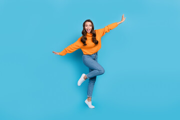 Fototapeta na wymiar Full length photo of childing fooling woman wear orange sweater having fun arms sides isolated blue color background