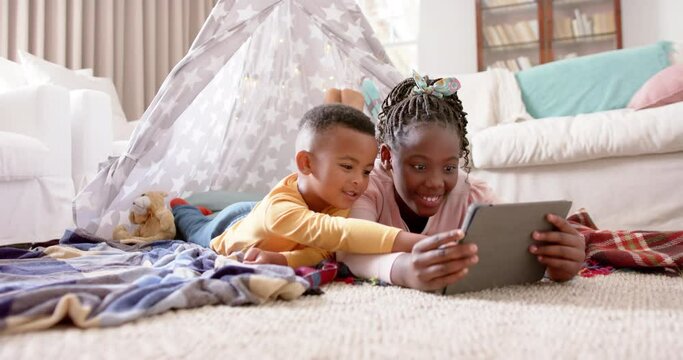 Happy african american sister and brother using tablet and smiling at home, slow motion