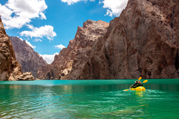 Kayaking on a mountain lake. Two men are sailing on a red canoe along the lake along the rocks. The theme of water sports and summer holidays.