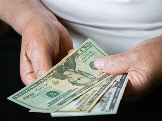 Hands of an old woman holding small US dollar bills. Front view