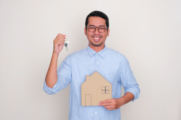 Adult man showing happy expression while holding a house key - obrazy, fototapety, plakaty