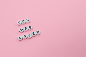 Top view of "you are loved" quotes made out of beads on pink background. motivation and success concept