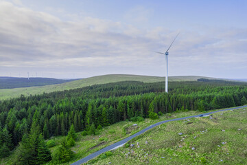 Fototapeta na wymiar Aerial view on a wind farm turbine build in a rural country area with green forest. Making power using power of nature. Blending technology into nature environment. Cloudy sky. Electricity production