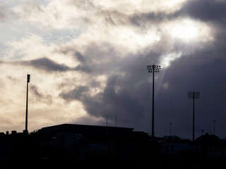 Silhouette of a stadium and tall lights on a pole against dramatic storm sky.